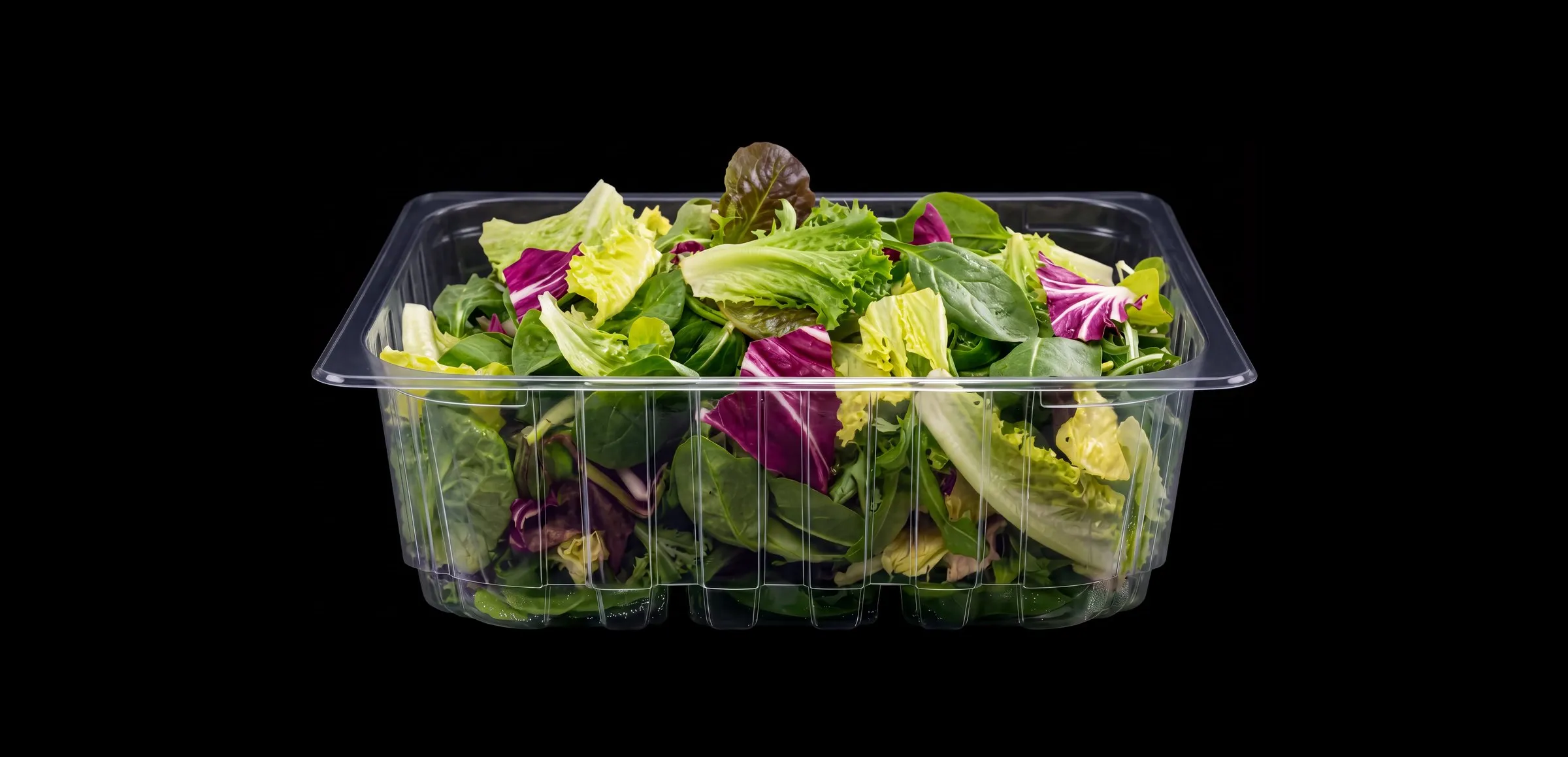 Clear container on black filled with mixed leafy greens